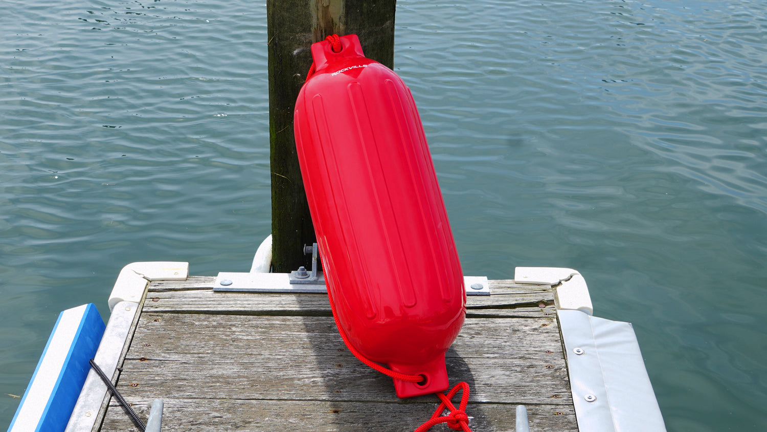 Red fender attached to a wooden dock with water in the background